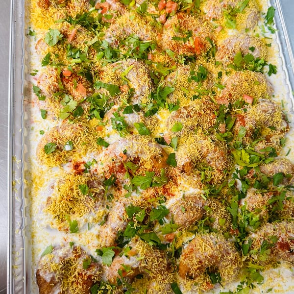 A tray of dahi vada, topped with yogurt, spices, sev, and fresh cilantro.