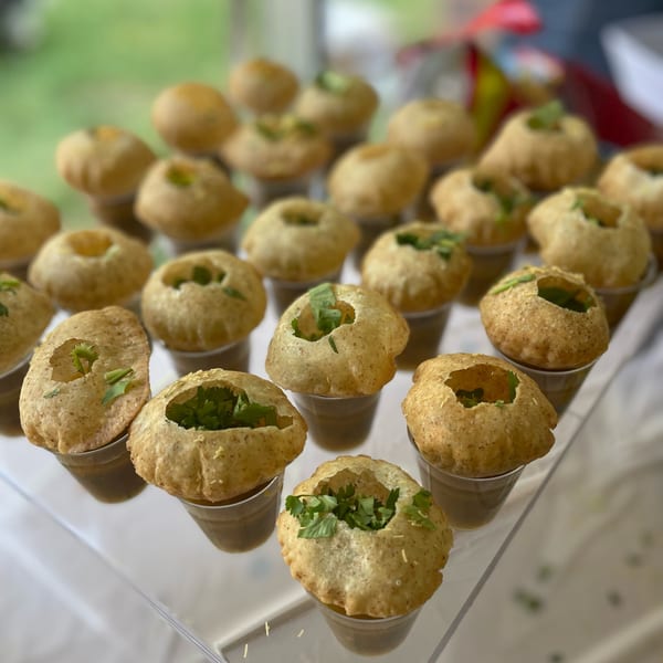 Numerous pani puri, crispy hollow balls filled with herbs and liquid, arranged on a clear tray.