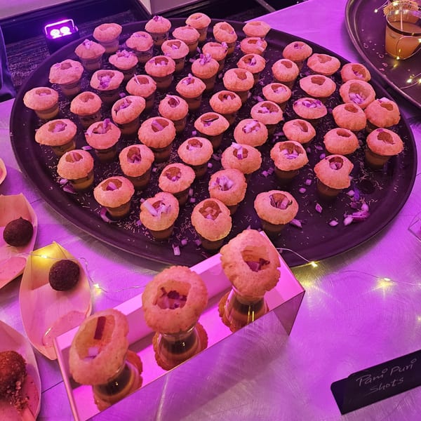 A black tray filled with Pani Puri shots, each with a crispy shell and diced onions.