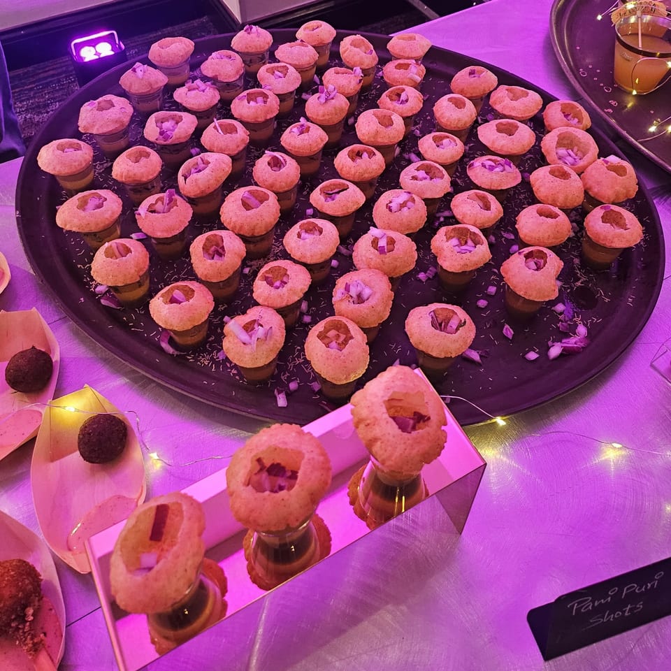 A black tray filled with Pani Puri shots, each with a crispy shell and diced onions.
