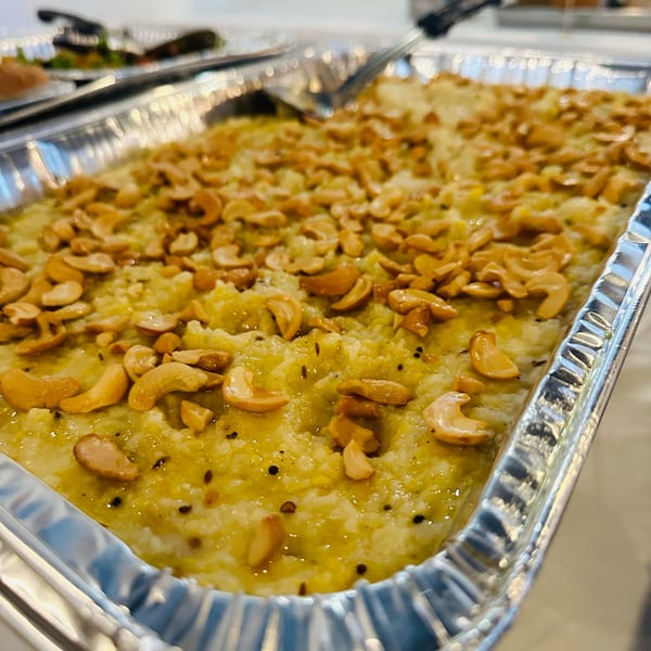 A close-up of a large foil tray filled with a yellow, granular dish topped with cashews.
