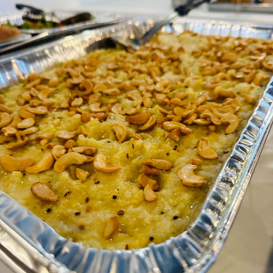 A close-up of a large foil tray filled with a yellow, granular dish topped with cashews.