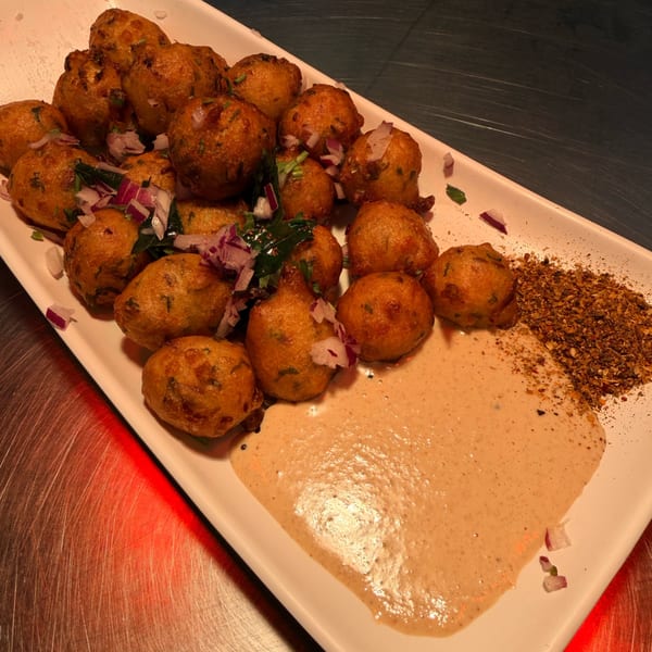 Crispy golden-brown fried fritters topped with red onions, served with a creamy sauce and spices.
