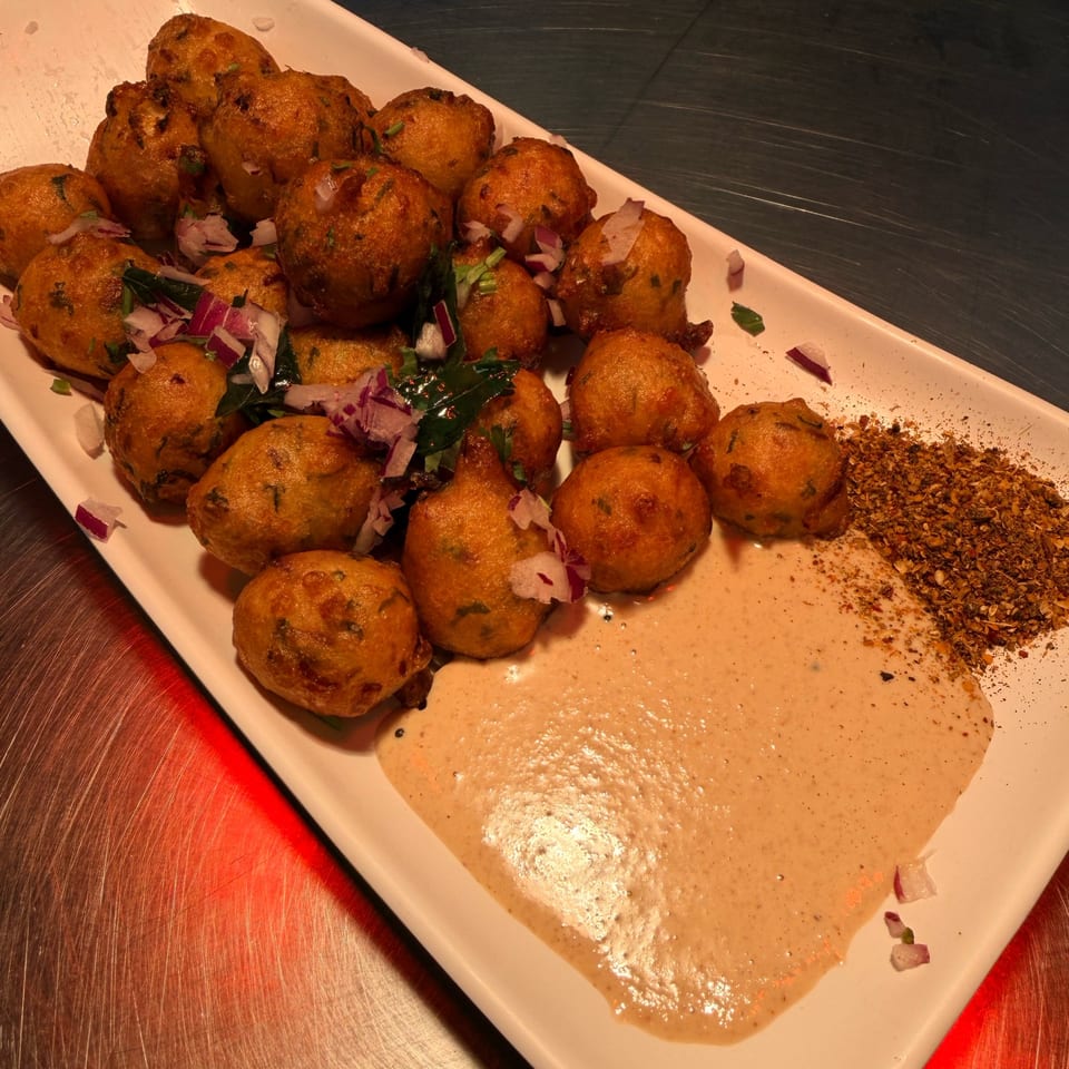Crispy golden-brown fried fritters topped with red onions, served with a creamy sauce and spices.