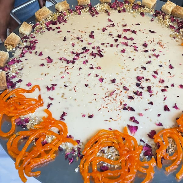 A large round platter of creamy dessert with orange jalebi, rose petals, and nuts.
