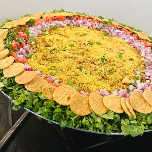 A large platter of colorful Indian chaat, with sev, chopped onions, tomatoes, and cilantro.