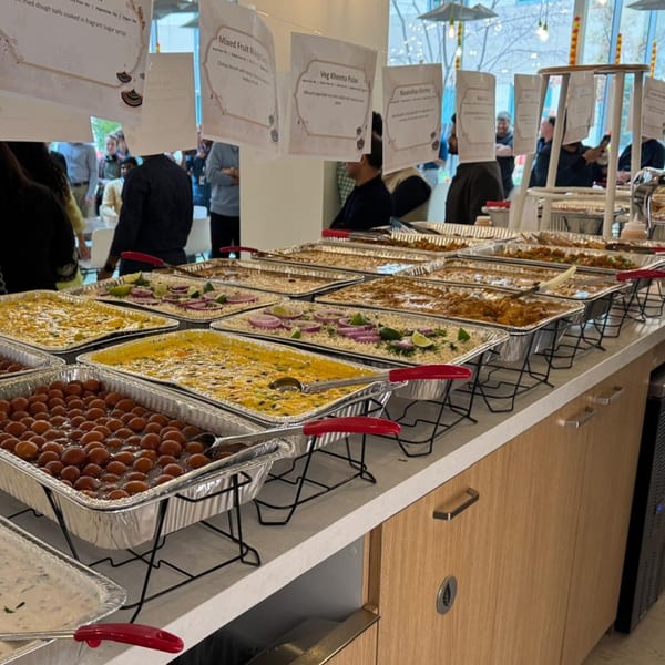 A buffet line with multiple trays of Indian food, including gulab jamun, rice, and curries.
