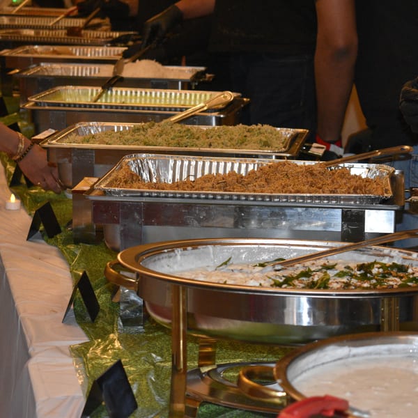 Buffet line with chafing dishes filled with rice and other dishes, a person serving.