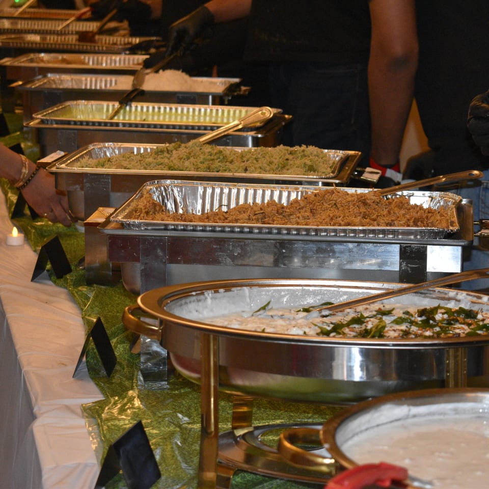 Buffet line with chafing dishes filled with rice and other dishes, a person serving.