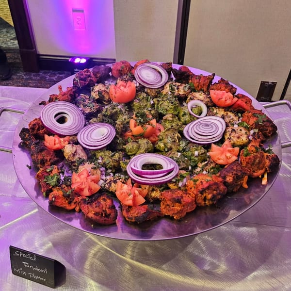 A large platter of tandoori chicken, green chicken, tomatoes, and red onions under purple lighting.