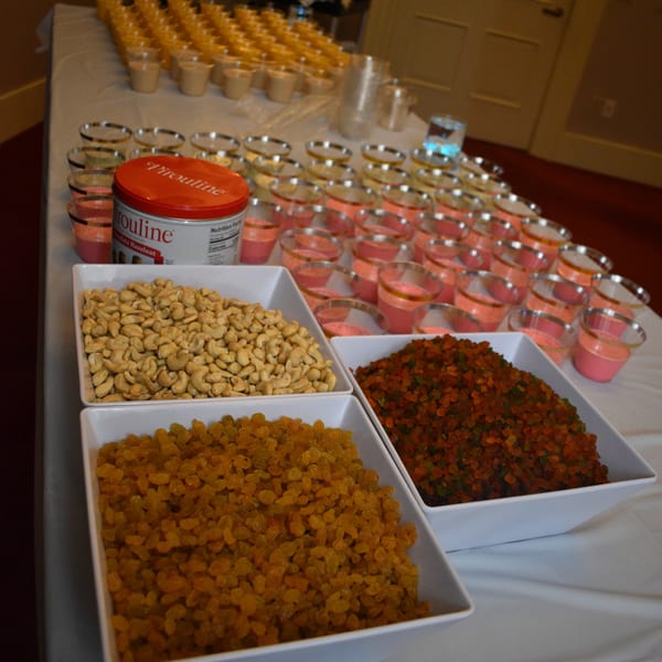 A table laden with small dessert cups, bowls of cashews, golden raisins, and candied fruit.